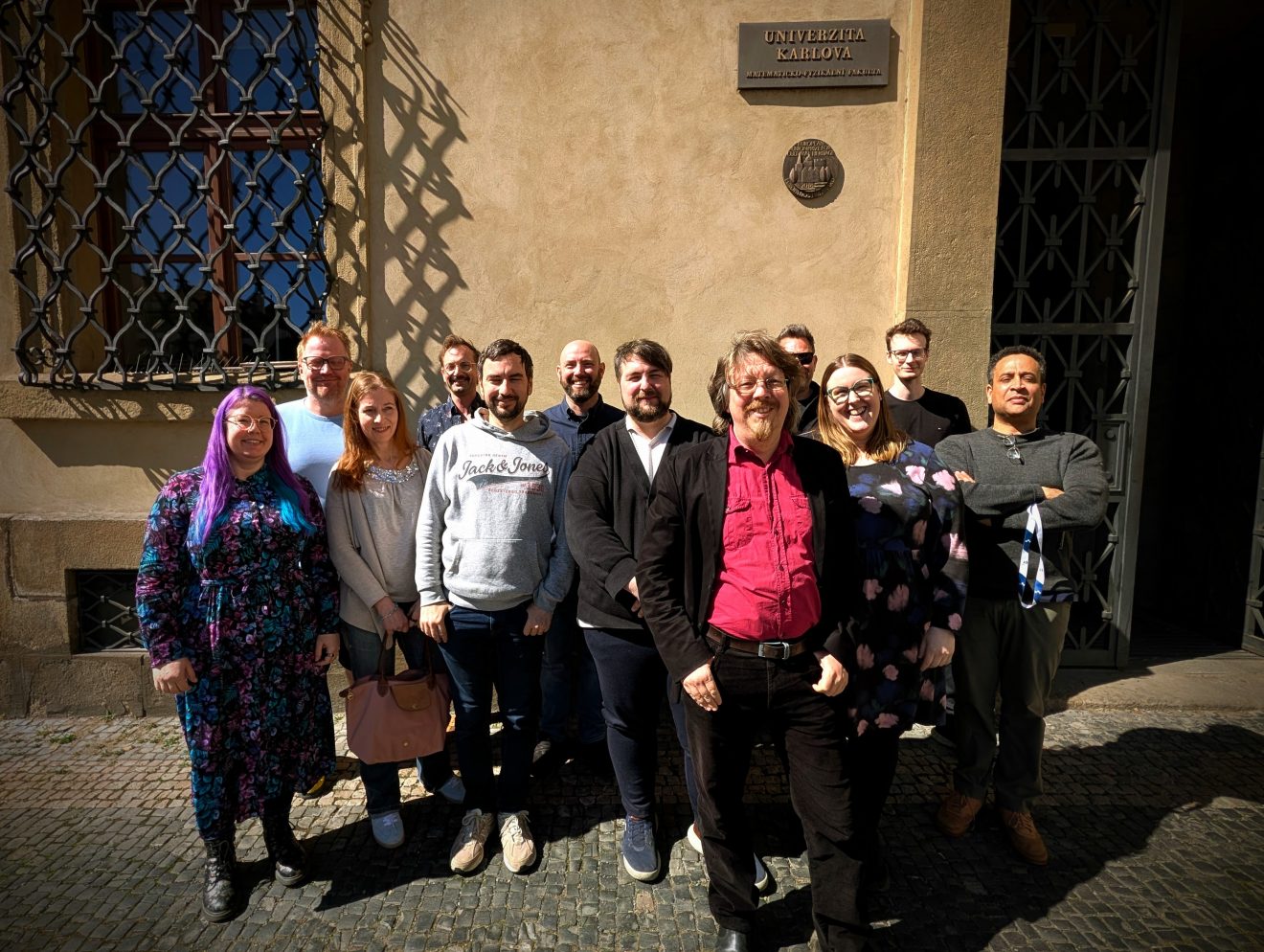 Group photo of people standing outdoors in front of a university building wall
