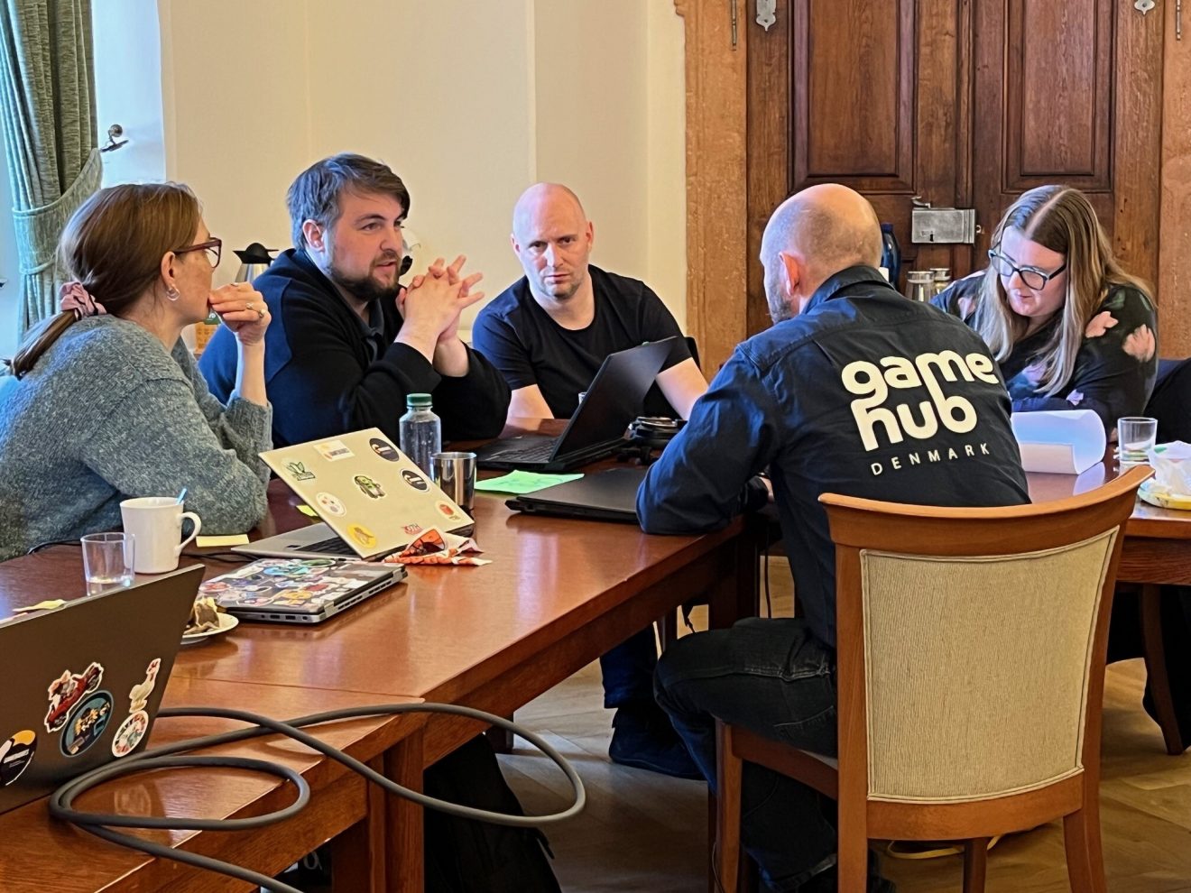 Group of people in a meeting around a table with laptops.